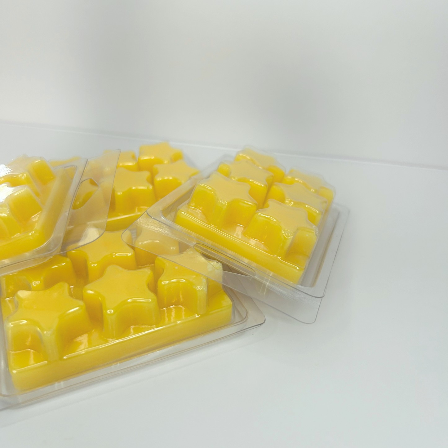 Four Lemon Sugar Cookie wax melt packs stacked and facing down, showcasing their yellow color and star-shaped plastic.