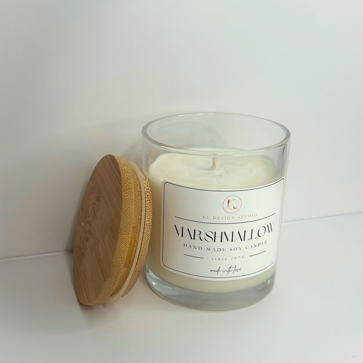 Side view of the 10oz Marshmallow Candle with the lid resting on the side, highlighting its inviting aroma and charming appearance.