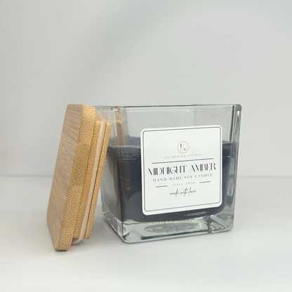 Angled view of the 10oz Midnight Amber Candle with the lid resting on the side, showcasing its dark black color and elegant design.