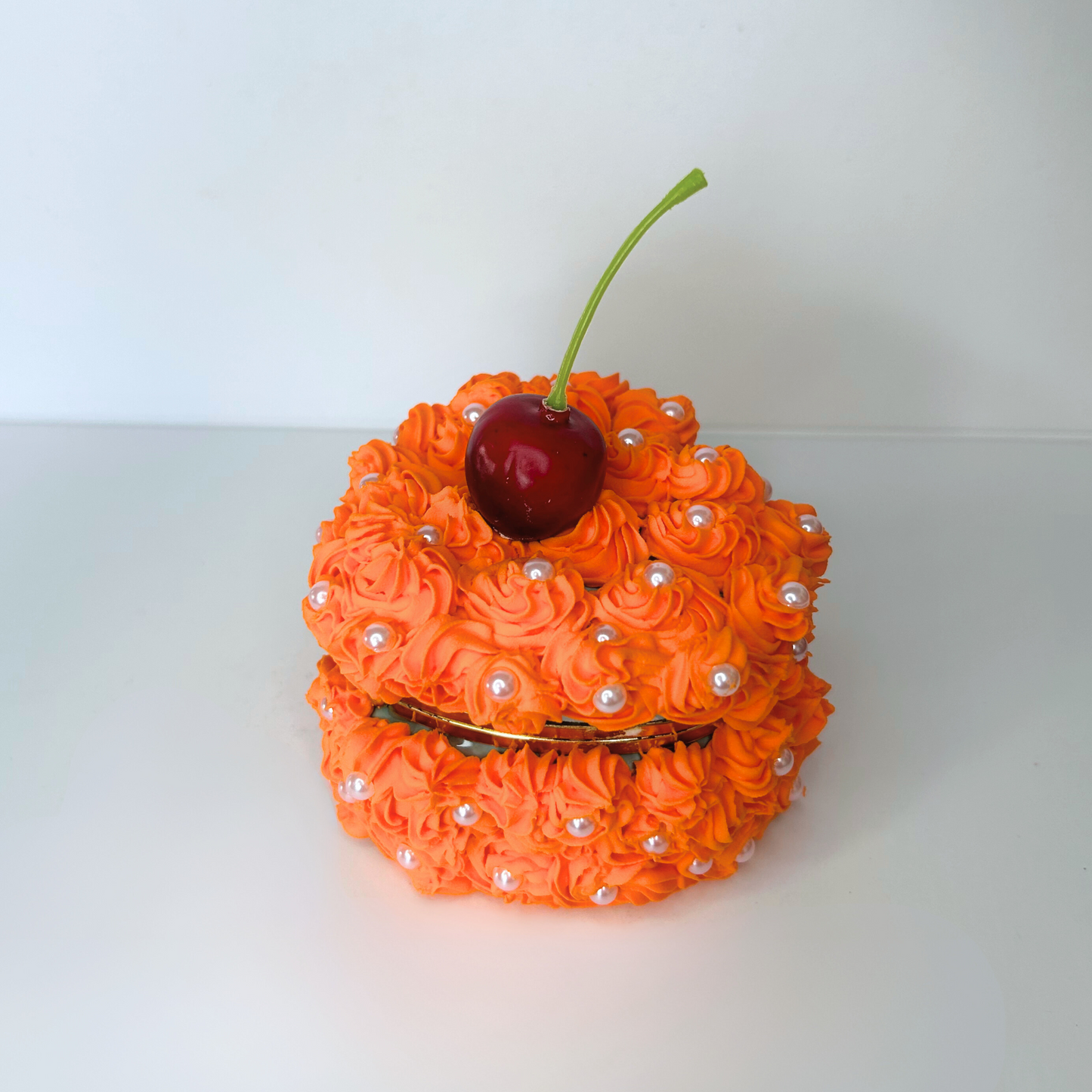 Angled view of the mini orange heart-shaped jewelry box, featuring swirly orange cream and a cherry, surrounded by white pearls for a charming, romantic design.