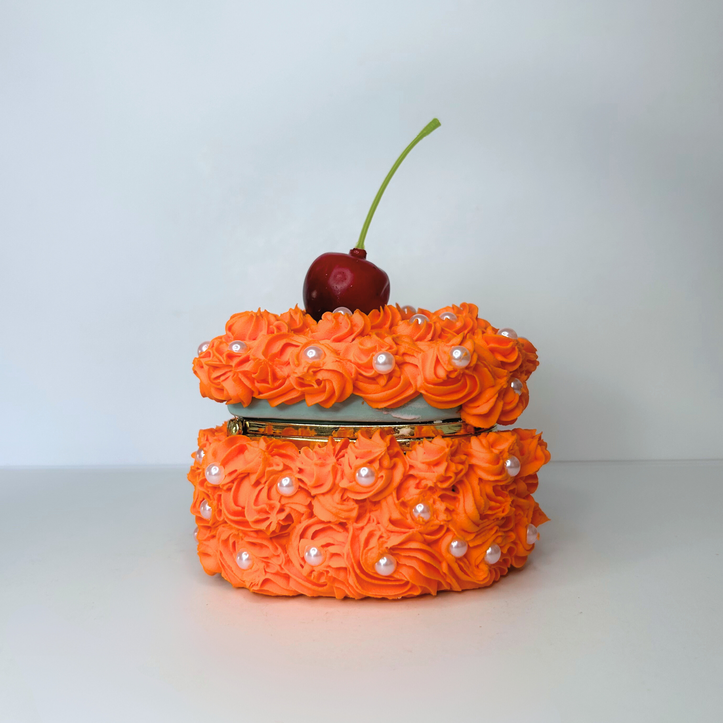 Side view of the mini orange heart-shaped jewelry box adorned with orange swirly cream and a cherry, with pearls adding elegance and sophistication.