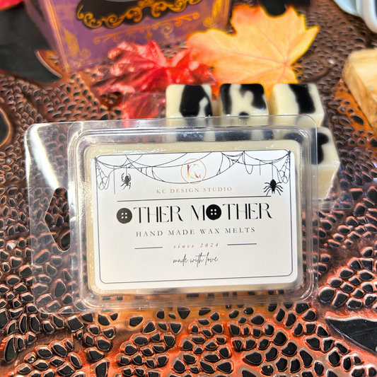 Other Mother hand-made wax melts packaging on a decorative surface with Halloween-themed elements.