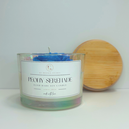 Front view of blue Peony Serenade Candle with soft floral notes and lid resting on the wall.