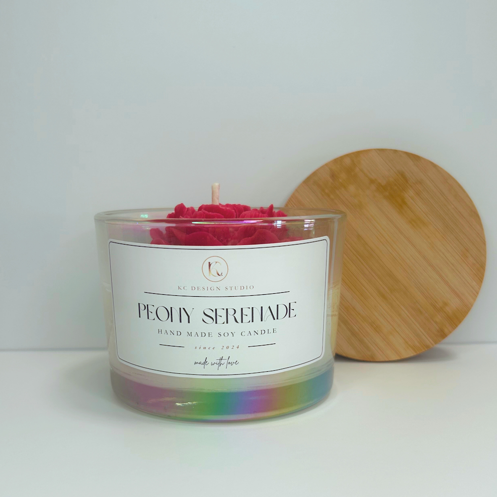 Front view of red Peony Serenade Candle with soft floral notes and lid resting on the wall.