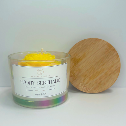 Front view of yellow Peony Serenade Candle with soft floral notes and lid resting on the wall.