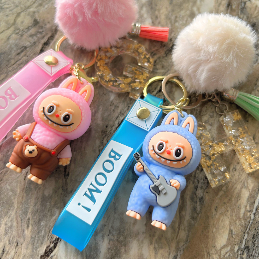 Custom Labubu doll keychains in pink and blue with personalized letters, pompoms, and tassels displayed together.