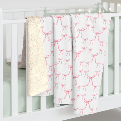 Pink bow Sherpa fleece blanket hanging from a bed, highlighting soft Sherpa backside and elegant pattern