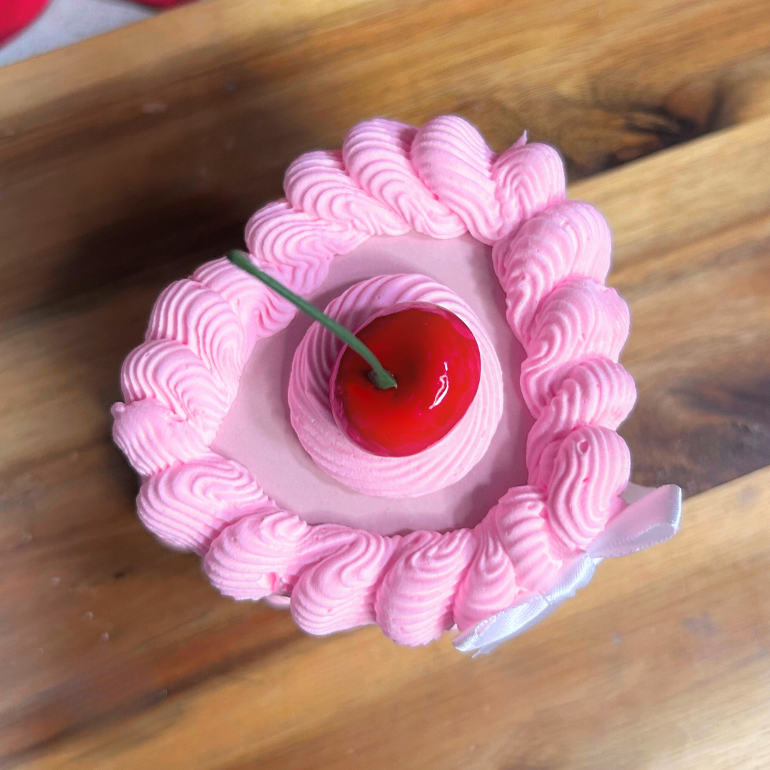 Pink whipped cream heart-shaped trinket box dessert with a cherry on top on a wooden surface.