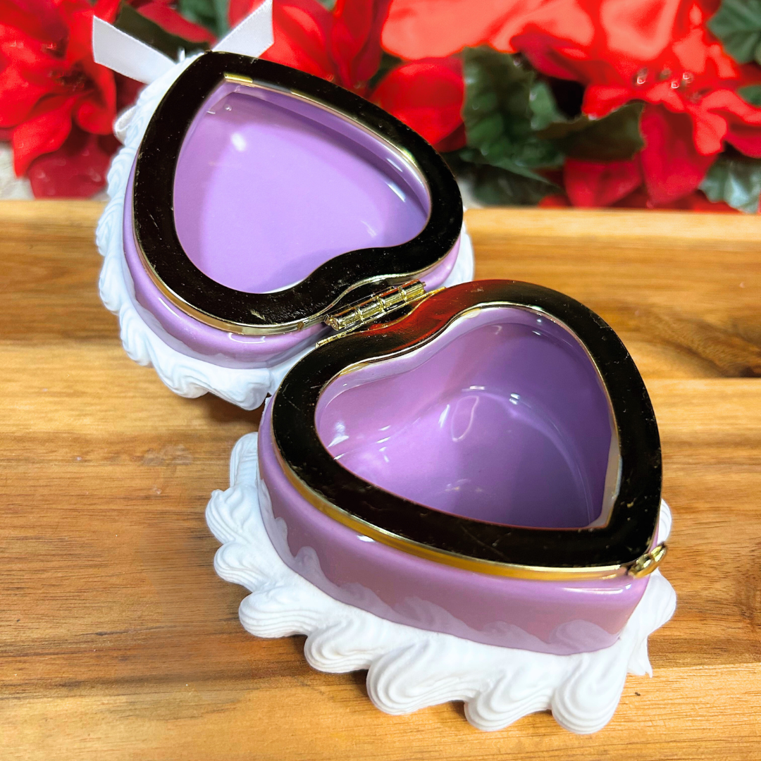 Heart-shaped purple jewelry box with gold rim on a wooden surface with red flowers in the background