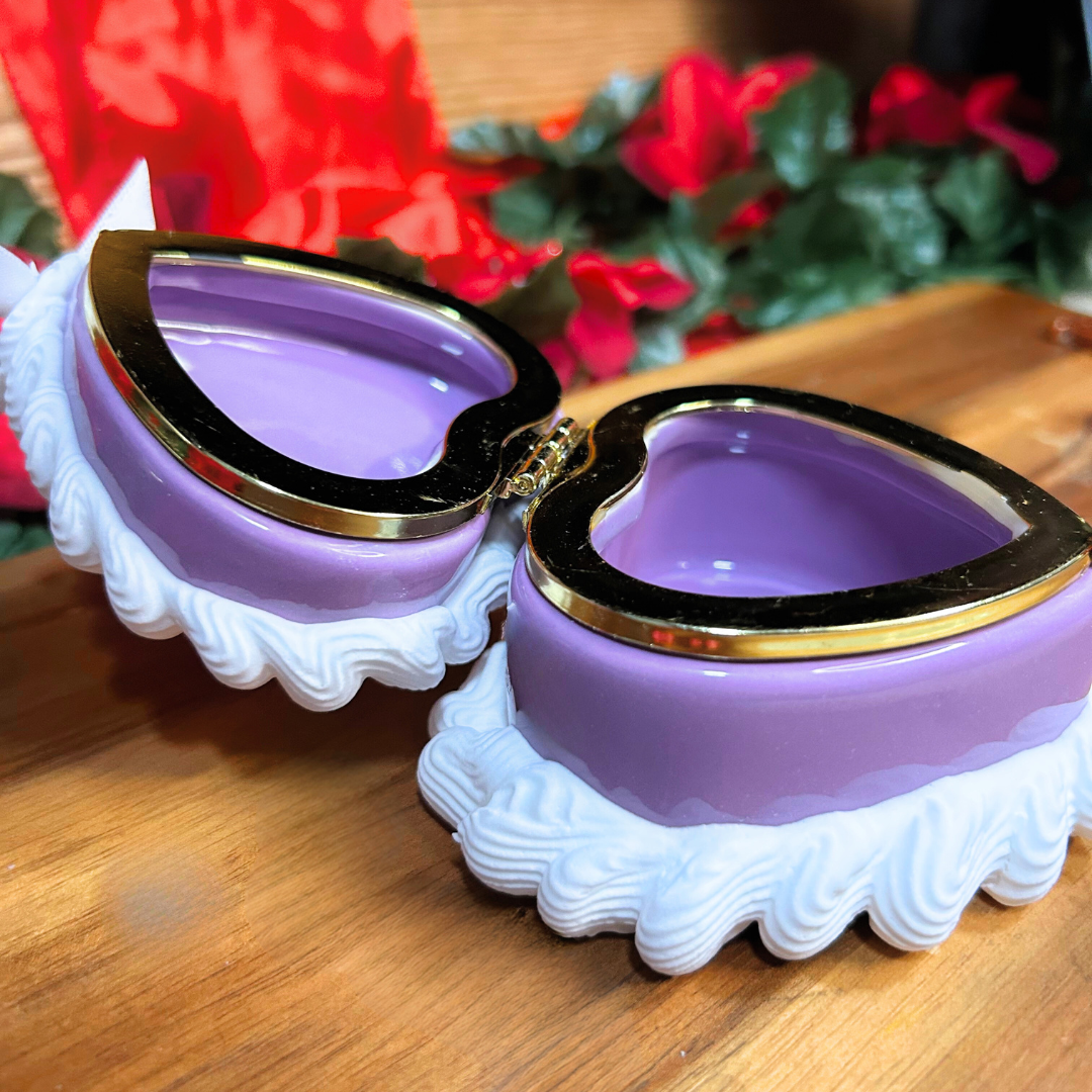 Heart-shaped purple and gold jewelry box on a wooden surface with flowers in the background