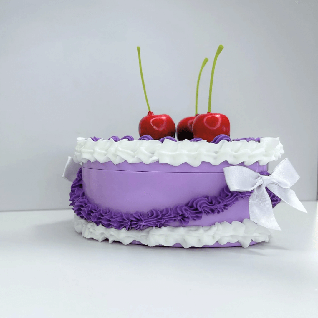 Side view of a whimsical heart-shaped jewelry box in purple and white cream, showcasing its vintage design and decorative cherries.