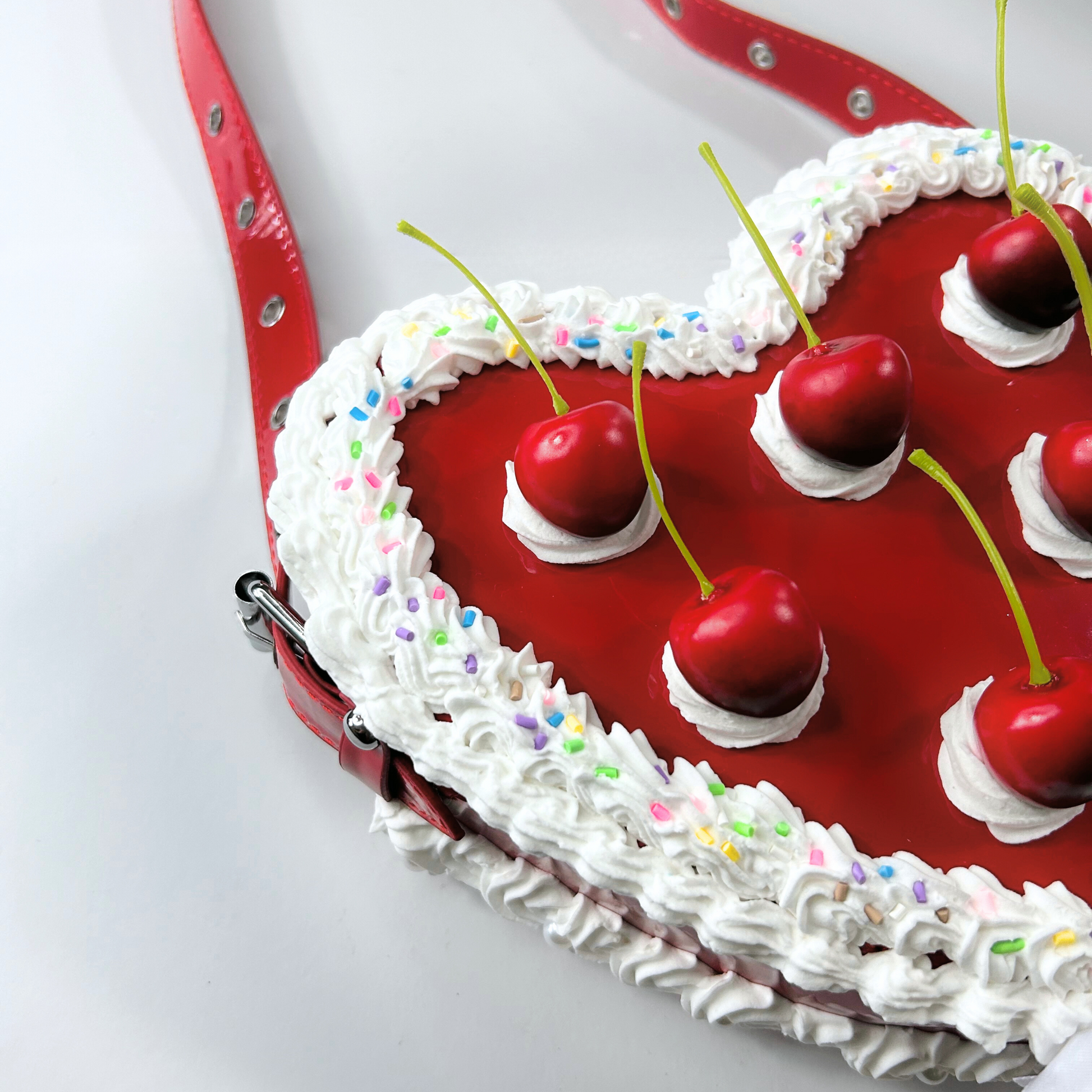 Angled view of a red vintage cake purse shaped like a heart, showing the cherry topper and side frosting details.