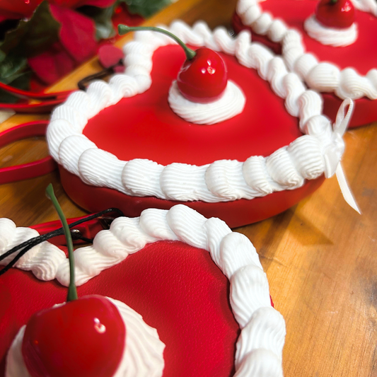 Red heart-shaped cake wrist bags with white frosting and cherries on a wooden surface