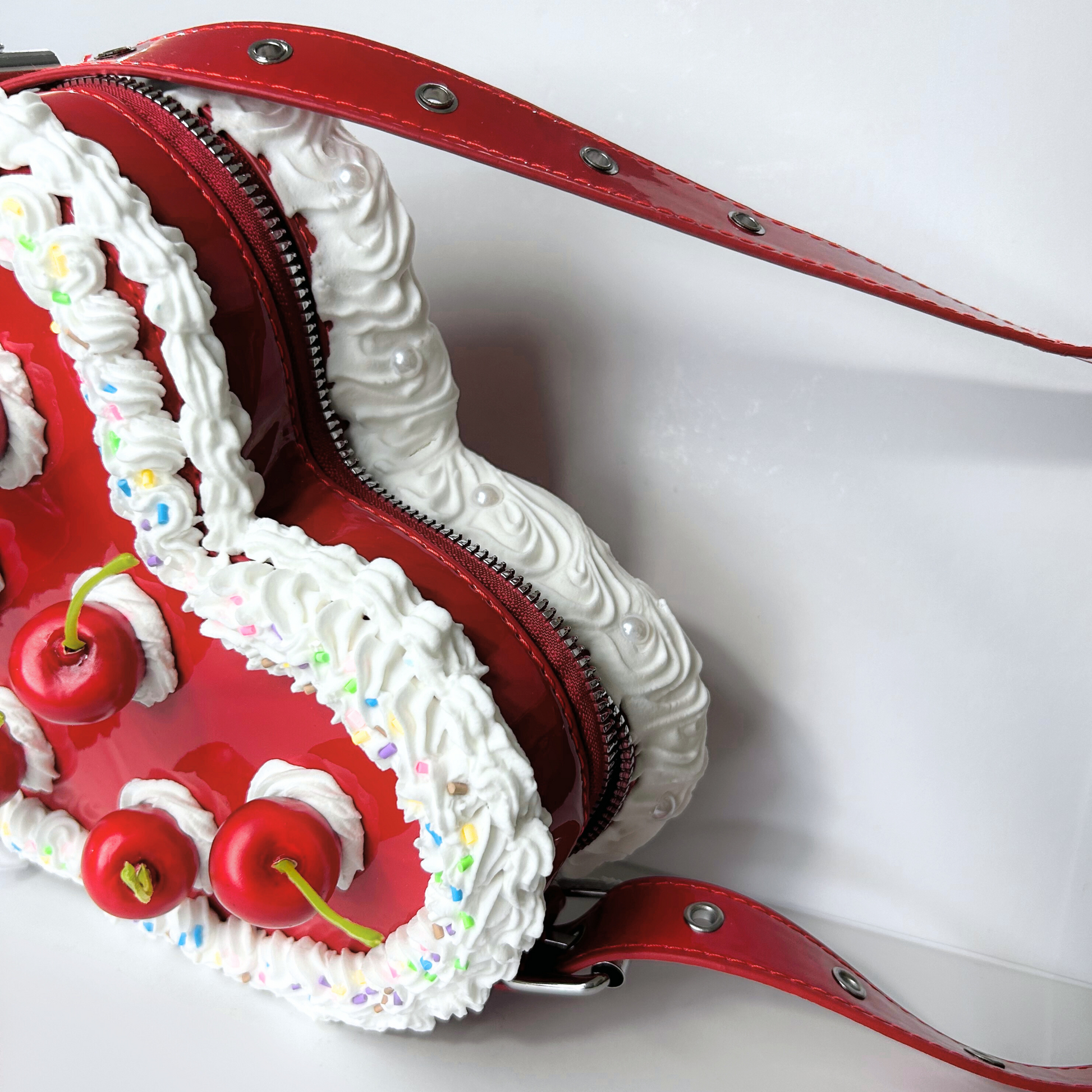 Side view of a red heart-shaped cake purse with a vintage look, showing the layered frosting details along the edge and a cherry accent on top.