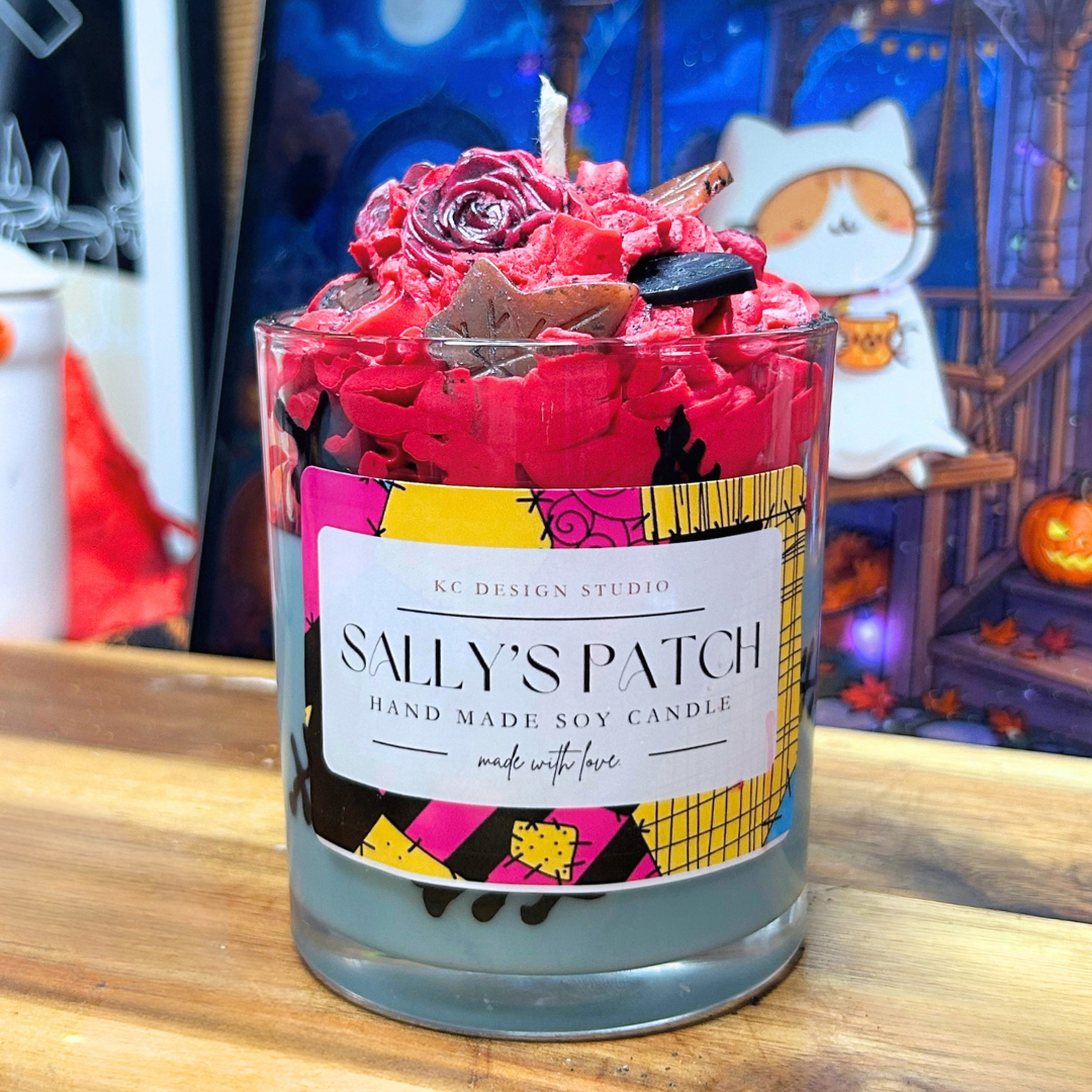 Sally’s Patch Candle with a light blue soy wax base, hand-drawn wax stitches around the glass, and red whipped wax topped with leaves and roses dusted with black mica powder.