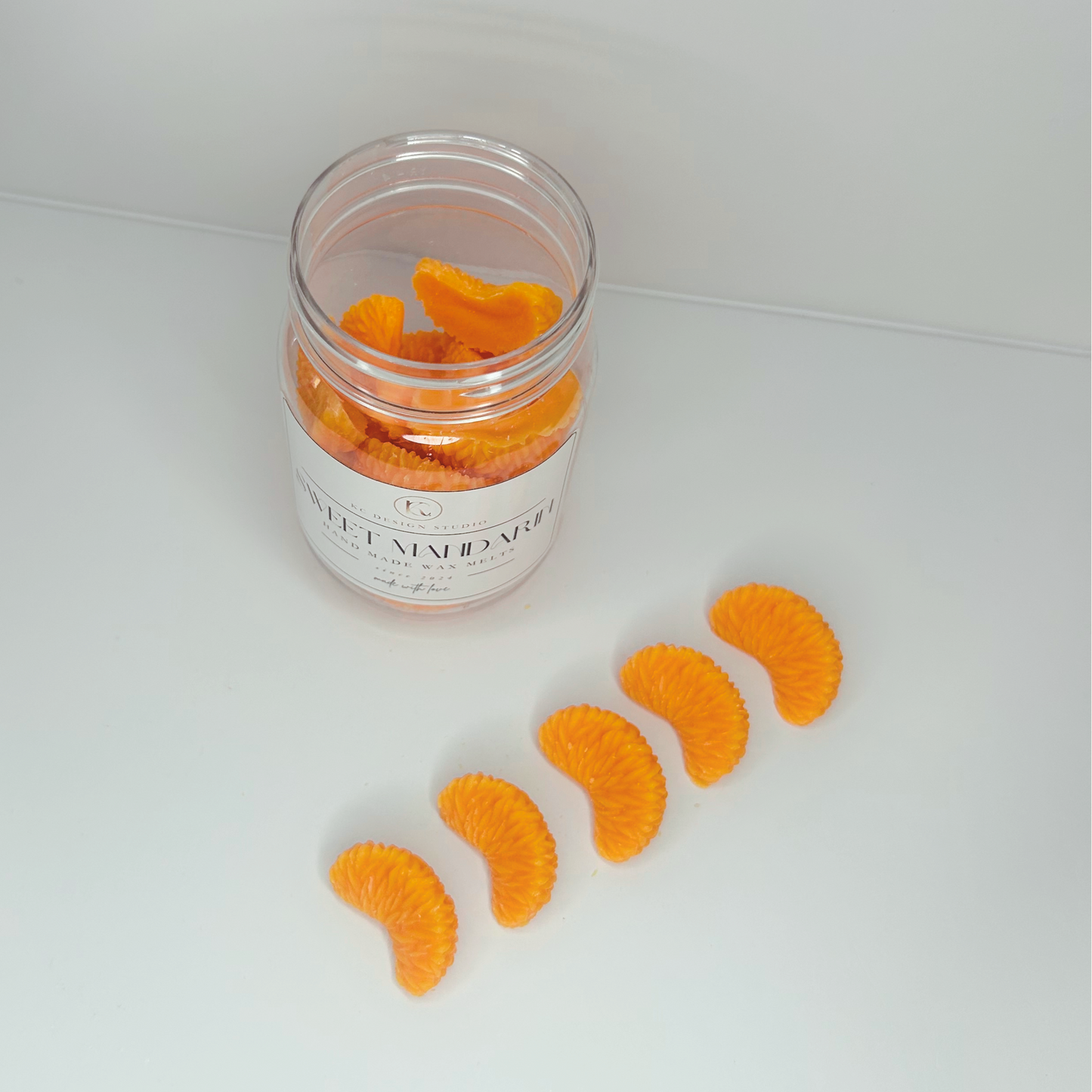 Top view of Sweet Mandarin wax melt jar and lined-up melts, displaying the arrangement and vibrant colors of the product.