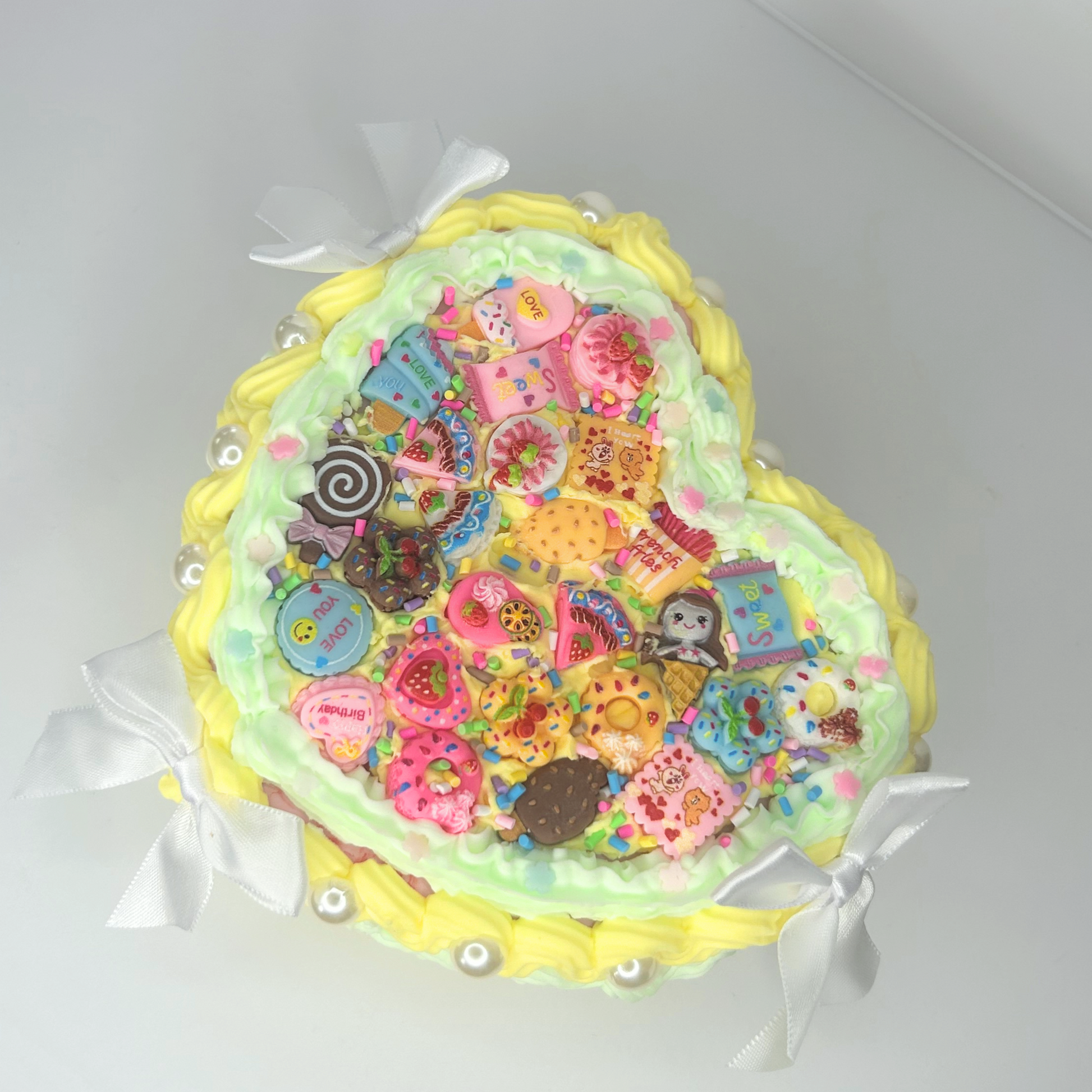 Top view of kawaii heart-shaped jewelry box with yellow and green colors, featuring pearls, mini white bows, and kawaii charms.