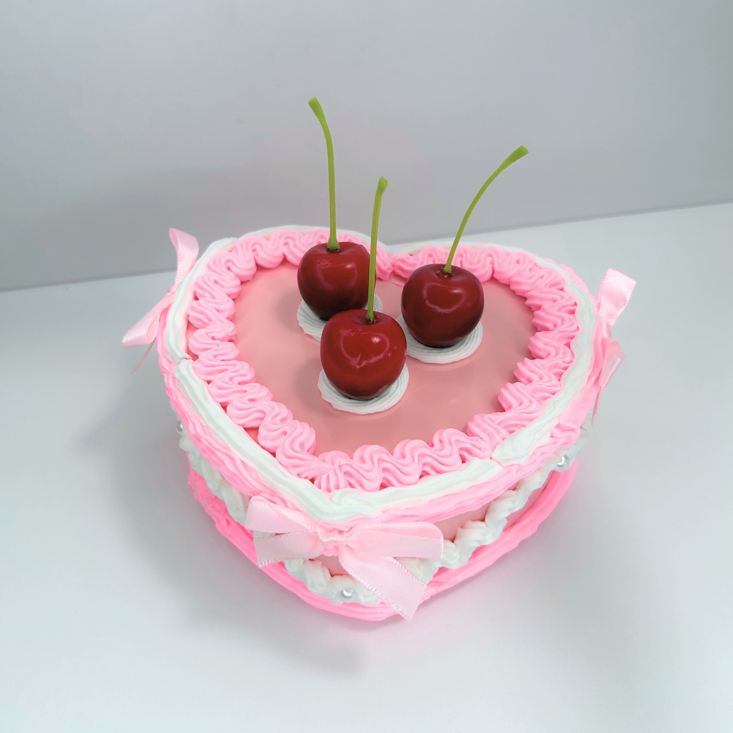 Top view of a pink and white jewelry box adorned with three cherries, pearls, and mini pink bows, showcasing its charming design and elegant color combination.