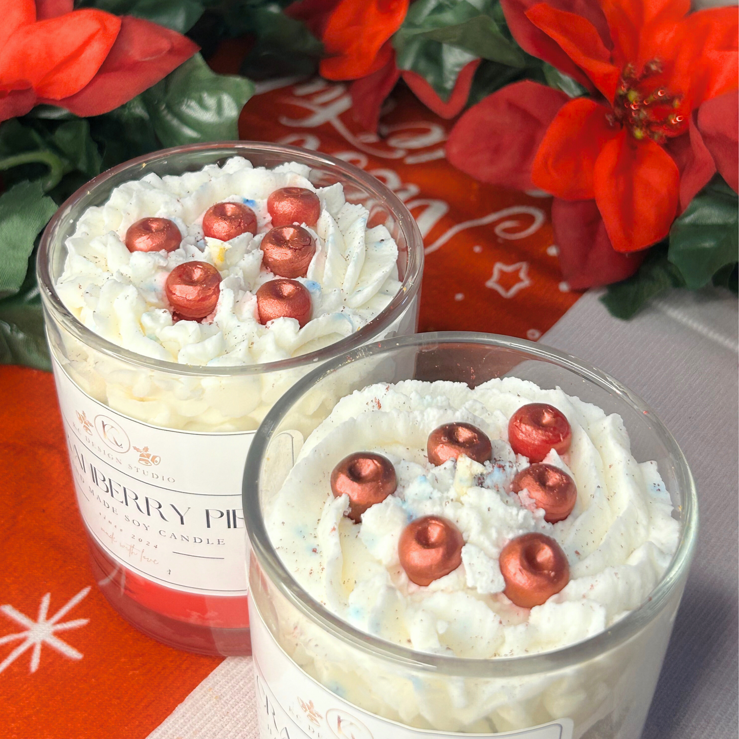 Top view of two cranberry pie candles with decorative Christmas-shaped cranberry toppings and whipped cream swirl.