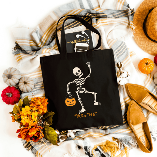 Black Trick or Treat Halloween Tote showcasing a spooky skeleton with a pumpkin basket design, ideal for festive Halloween adventures.