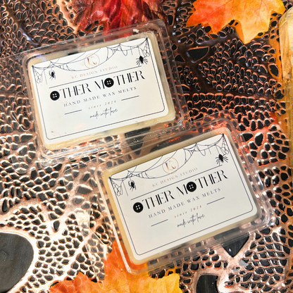 Two wax melts in clear packaging with 'Other Mother' text on a textured surface with autumn leaves.