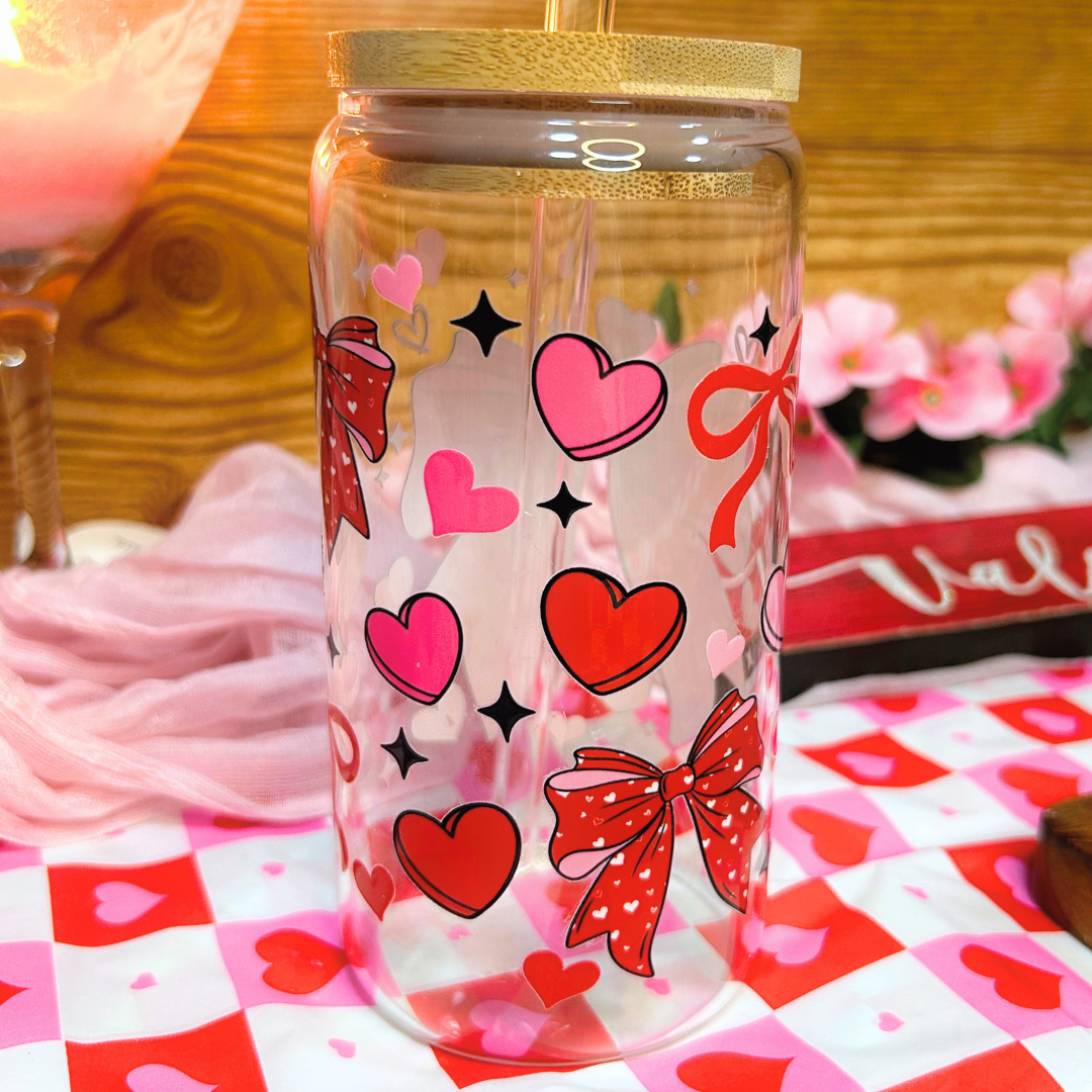 Clear glass jar with red and pink heart and bow designs on a checkered tablecloth.