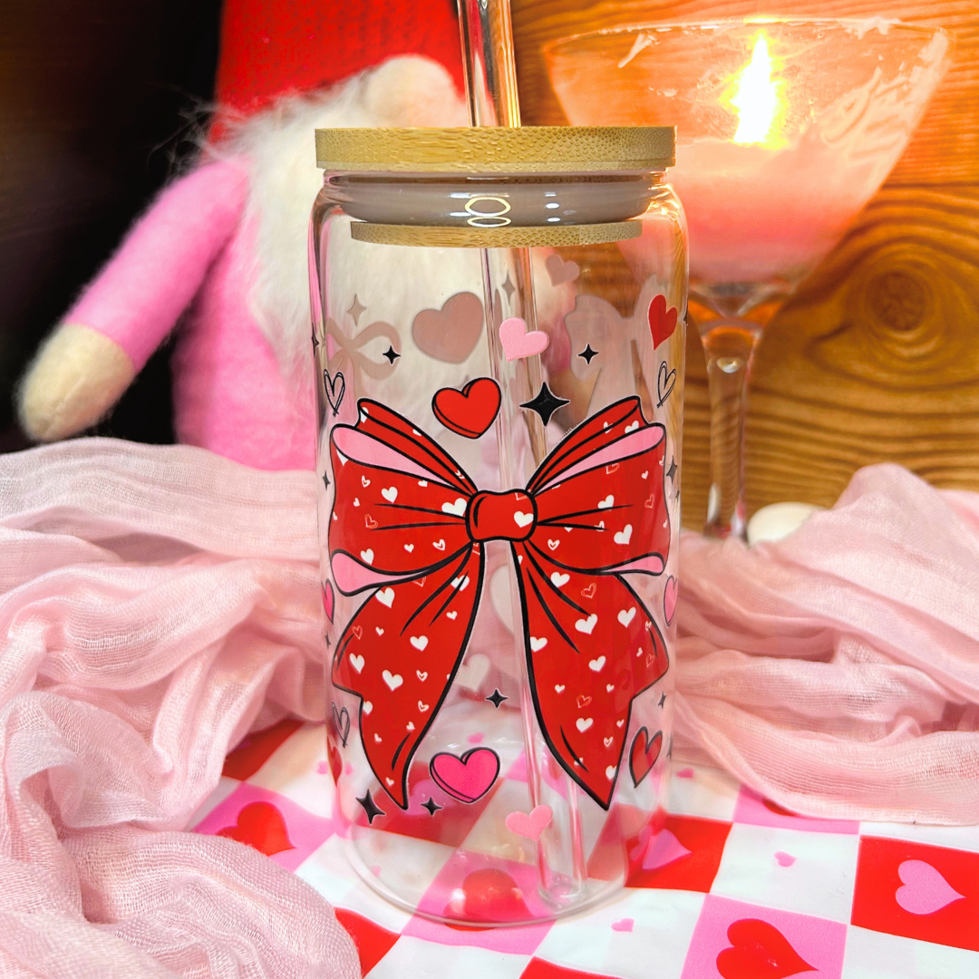 Clear tumbler with a red bow design on a checkered tablecloth with pink hearts.