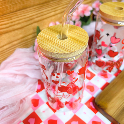 Clear tumbler with red heart designs and a wooden lid on a checkered tablecloth.