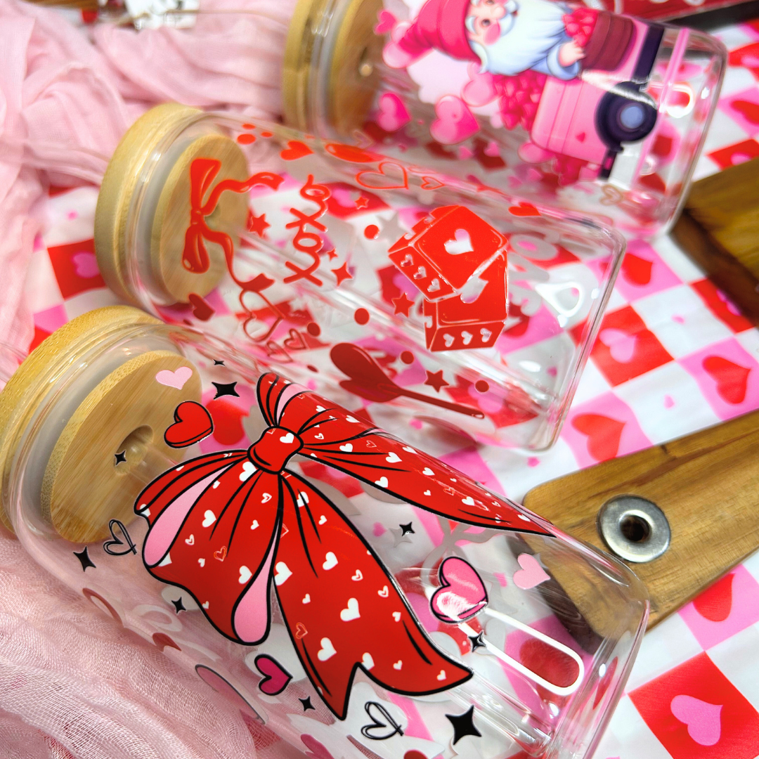 Clear glass bottles with red bow and heart designs on a pink and white heart-patterned background.
