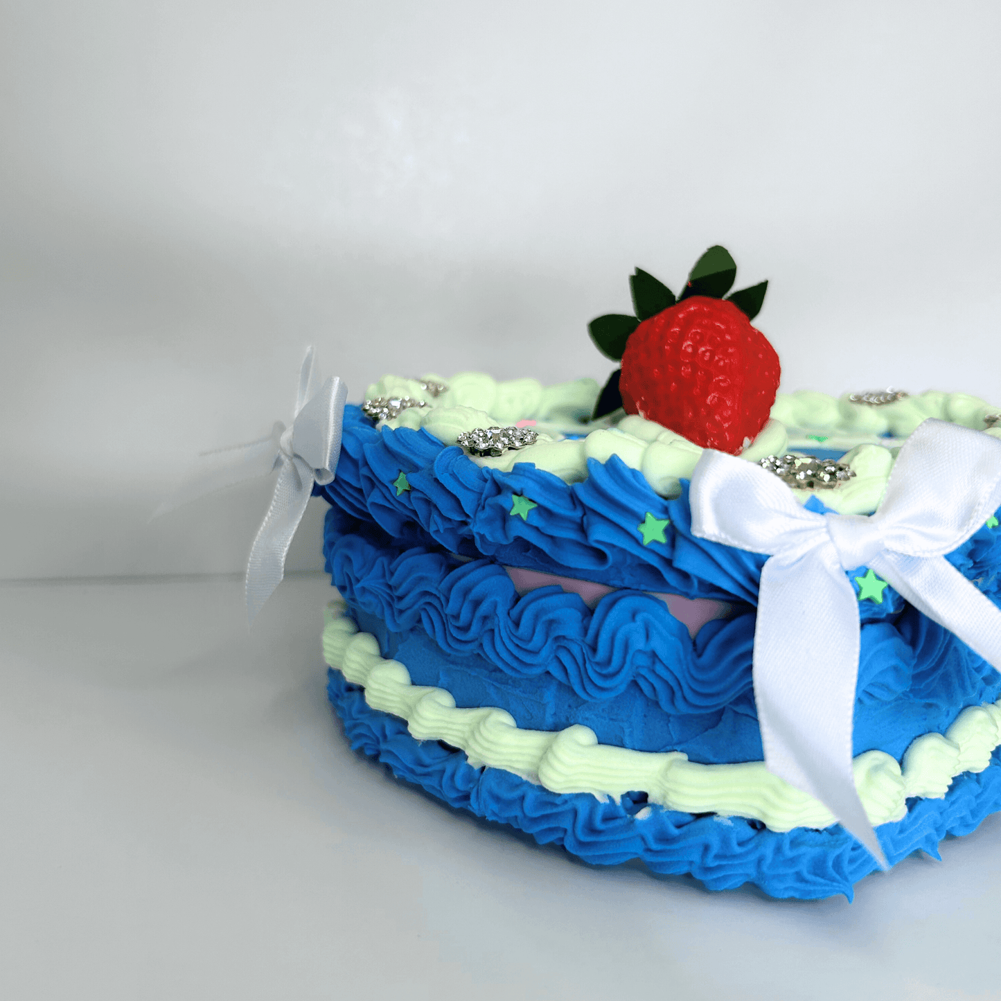 Close-up of the intricate details on a heart-shaped vintage jewelry box, highlighting the blue and green cream, strawberry in the center, flower toppings, and decorative white bows.