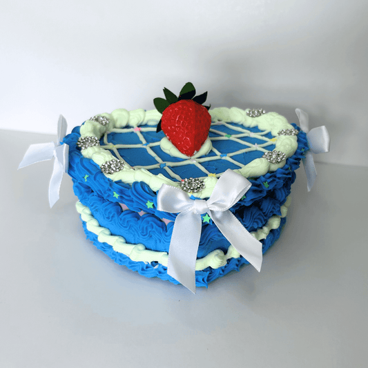 Front view of a heart-shaped vintage jewelry box with a blue and green cream design, featuring a strawberry centerpiece and three white bows.