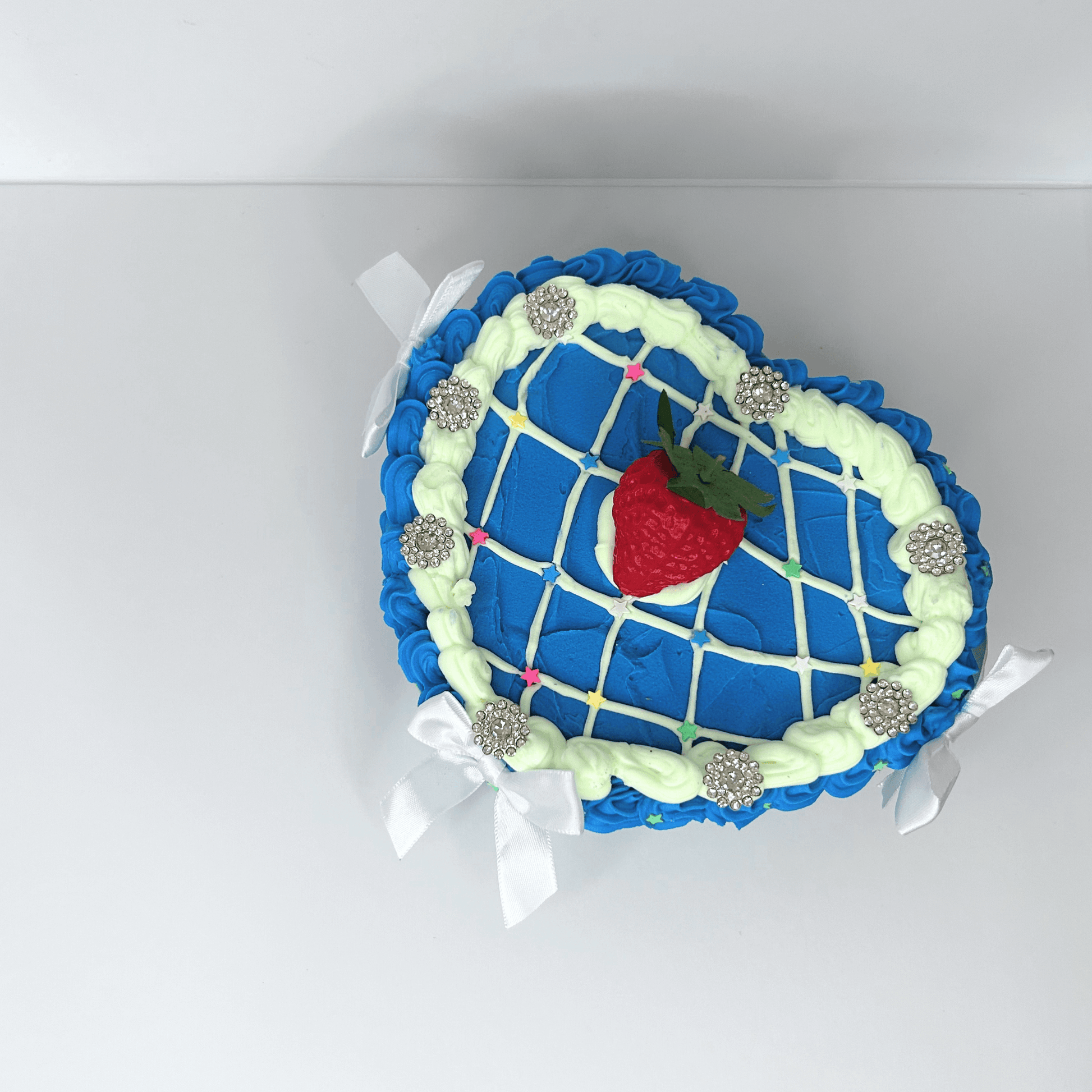 Top view of a heart-shaped vintage jewelry box showcasing the blue and green cream design, floral toppings, and a central strawberry.