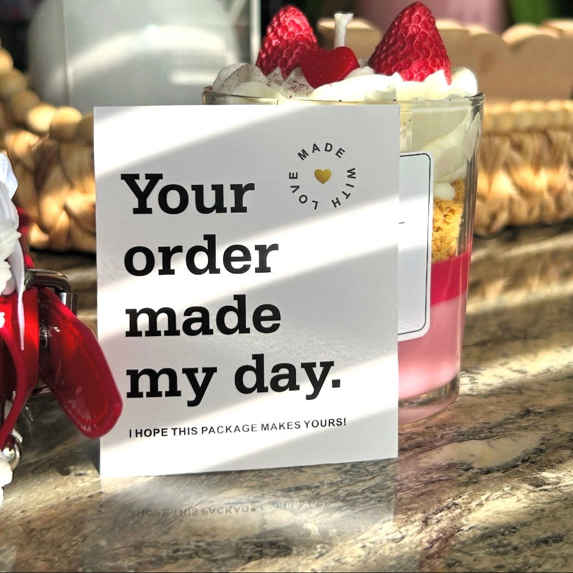 Candle with a "Your order made my day" card on a marble surface.